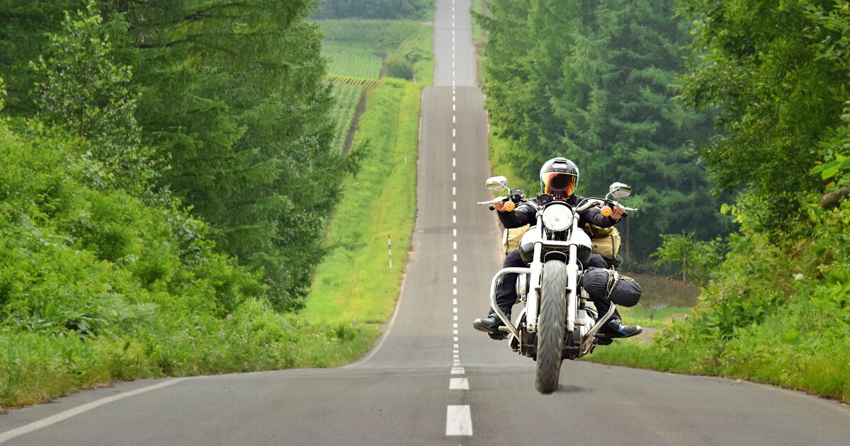 森林に囲まれたアップダウンの道を走る白いバイク