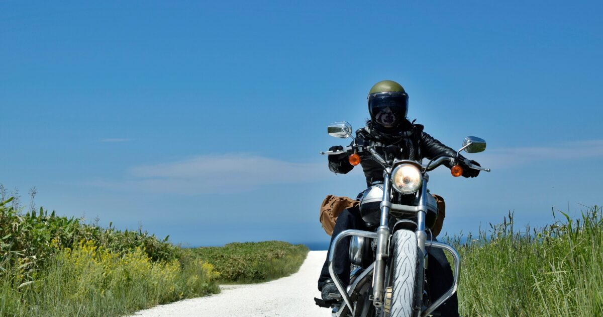 青空と海を背景に走るバイクライダーの正面ショット