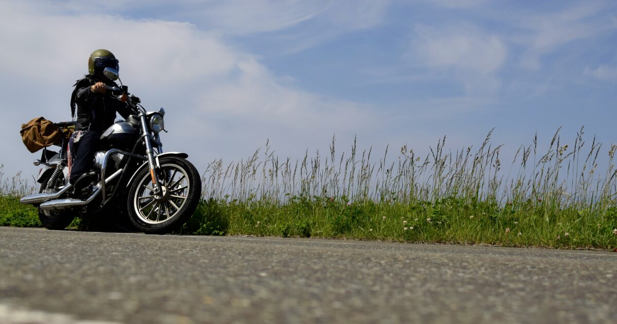 道端に停車するバイクとライダーと草花の風景